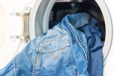 Open door in washing mashine with jeans inside close upの写真素材