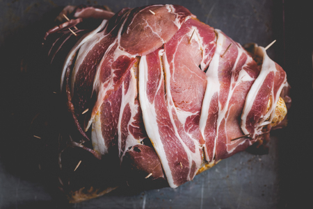 Large turkey wrapped in bacon slices on vintage silver roast pan in dull faded dark lightの写真素材