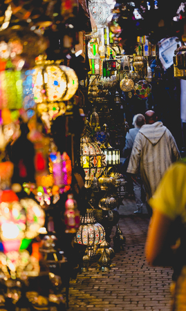 Old medina souk market in Marrakesh, Morocco. Berber man in background wearing traditional coat. Path with colourful lamps. Vertical cropの写真素材