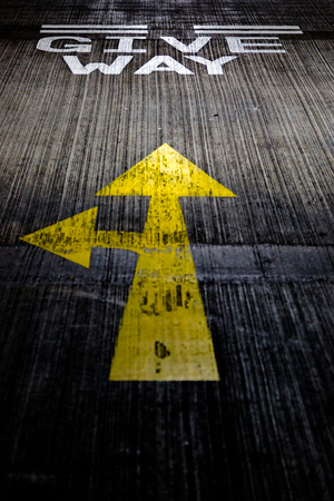 Give way yellow arrows painted on concrete road on car park floor. Dramatic dark tones vertical cropの写真素材