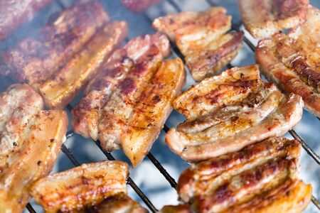 Grilled pork belly, bacon, on hot traditional charcoal bbq close up. Horizontal macro shot