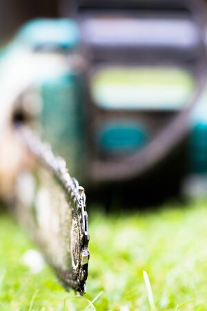 Dirty in sawdust chain saw on grass in garden close up. Vertical low angle perspective crop with shallow depth of fieldの写真素材