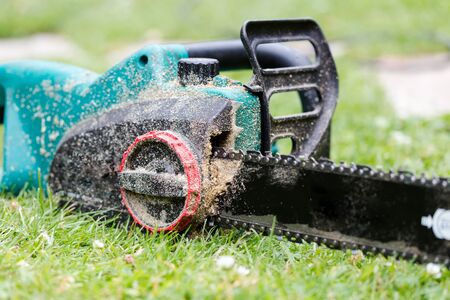 Dirty in sawdust chain saw on grass in garden close up. Horizontal side low angle perspectiveの写真素材