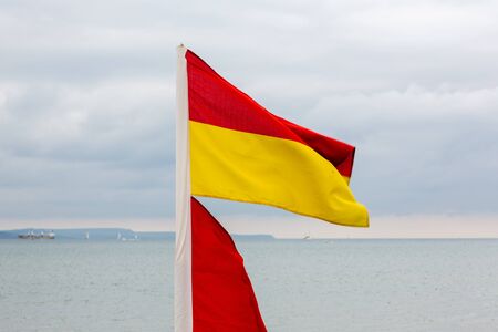 Red and yellow lifeguards flag on beach. Dramatic sky with clouds in backgrounds.の写真素材