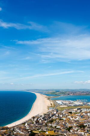 Aerial view on Chesil Beach, marina and Fortuneswell town on Isle of Portland, UK. Vertical crop, low horizon. Sunny day, blue sky and azure waterの写真素材