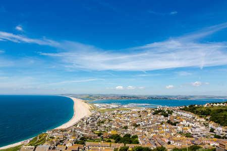 Aerial view on Chesil Beach, marina and Fortuneswell town on Isle of Portland, UK. Horizontal crop, low horizon. Sunny day, blue sky and azure waterの写真素材