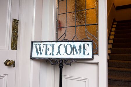 Vintage welcome message at etrance into old home. Horizontal crop in day light. Stairs in background