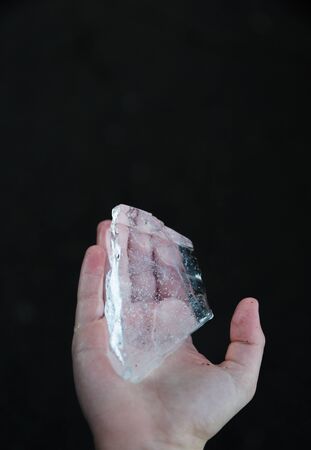 Pure clear transparentice cube on young boy hand. Top front view, black background.