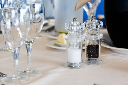 Luxury restaurant table with plates and glasses set. Close up crop, focus on glass salt shaker and...