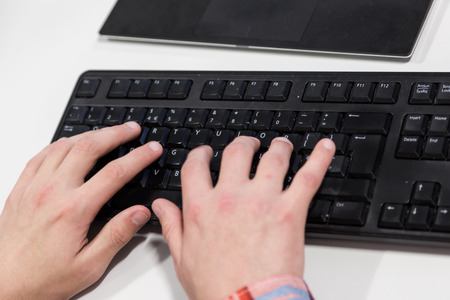 Young hacker typing code on computer keyboard. Close up crop. Focus on typing hands and keyboard.