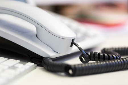Bright white office telephone station on desk. Close up macro view, low angle perspectiveの写真素材