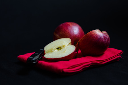 Vibrant red Royal Gala English apples on red tea towel with knife contrasting to black background. Macro close up crop with selective focus and shallow depth of fieldの写真素材