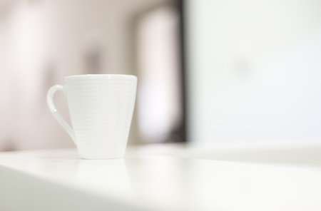 White coffee mug on counter desk in reception room  with real natural bright  daylight. Close up shot with focus on the tea mug with blurred backgroundの写真素材