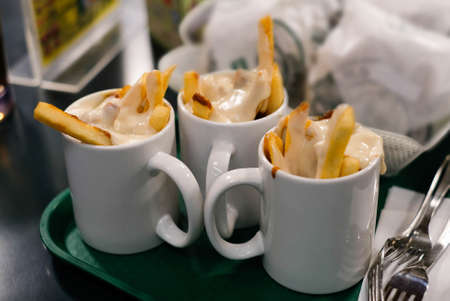 Cup of French fries with melted cheese on green tray.