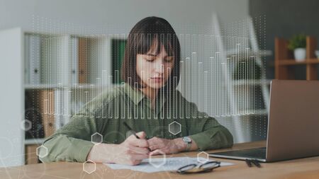 Businesswoman using laptop and writing in notebookの写真素材