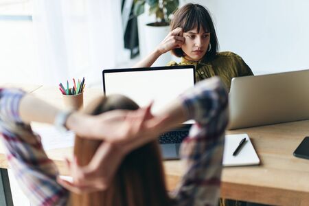 Back view of two young woman working in modern office using laptopの写真素材