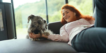 Beautiful redhead woman resting on a sofa laughing and cuddling a dog