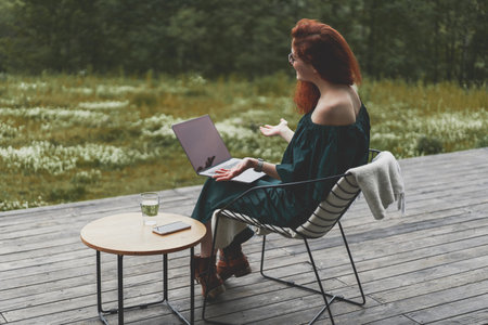 Back view of successful woman working with laptop and sitting outdoor in a beautiful terrace in forestの写真素材