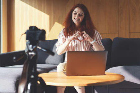 Front view of successful woman recording video lesson with digital camera, tripod and laptopの写真素材