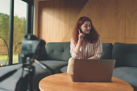 Successful business woman recording video with camera, tripod and laptopの写真素材