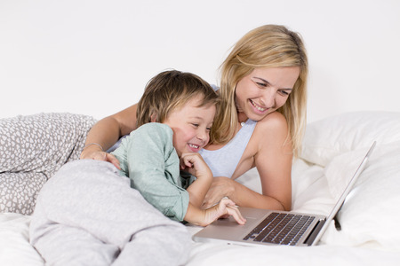 Mutter und Sohn liegen mit Notebook auf einem Bettの写真素材