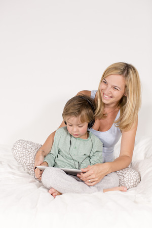 Mutter und Sohn sitzen mit Notebook und Kopfhörer auf einem Bettの写真素材
