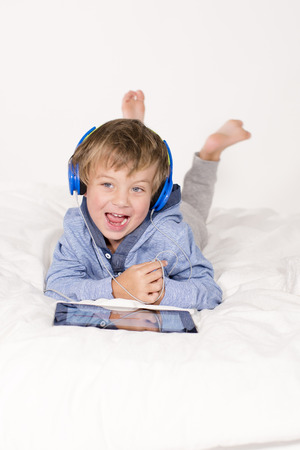 Young boy with tablet and headphones on a bedの写真素材