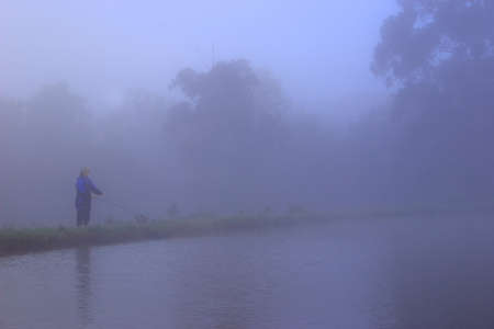 Lady fly fishing along the bank of a lake in the mist.の写真素材