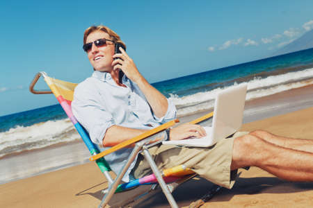 Business man calling by cell phone and working on computer at the beach in Hawaiiの写真素材