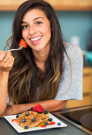 Young woman eating Waffles with Fresh Fruit, Breakfast at Home の写真素材