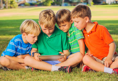 Group of kids on grass using tablet computerの写真素材
