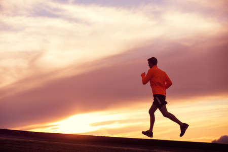Male runner silhouette, Man running into sunset, colorful sunset sky の写真素材