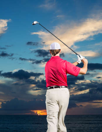 Golfer at sunset, Man swinging golf club with dramatic sunset sky backdropの写真素材