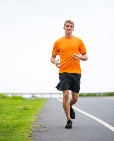 Athletic man running outside, training outdoors. Jogging on road 