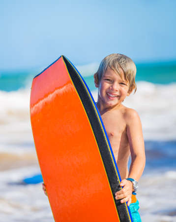 Happy Young boy having fun at the beach on vacation, with boogie board