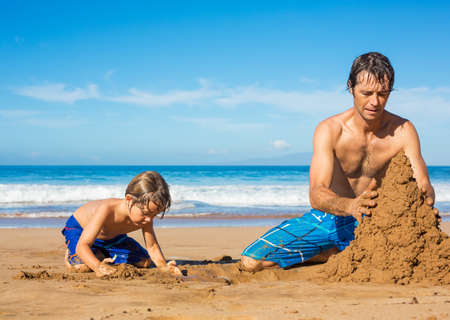 Father and son playing together in the sand on tropical beach, Building sand castleの写真素材