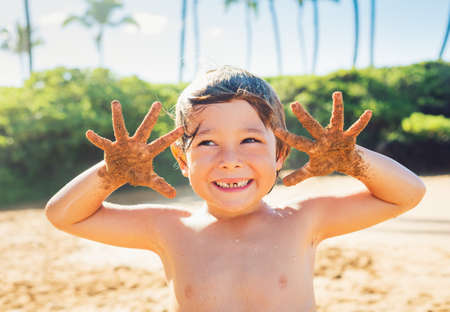 Happy young boy at the beach, smiling with sandy handsの写真素材