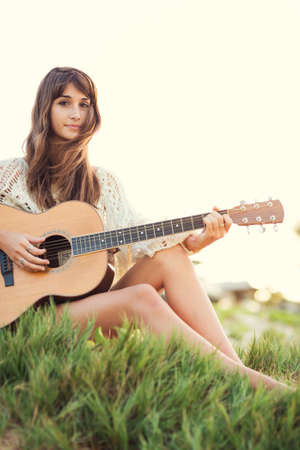 Beautiful young woman playing guitar on beach at sunset, fashion lifestyleの写真素材