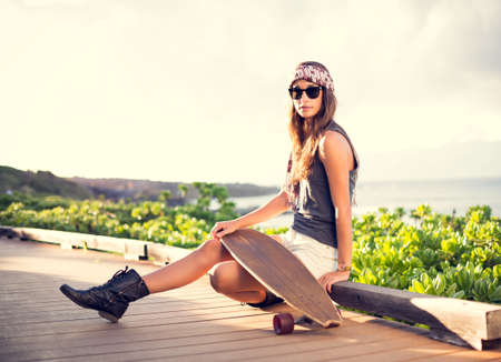 Fashion lifestyle, Beautiful young woman with skateboard, backlit at sunsetの写真素材