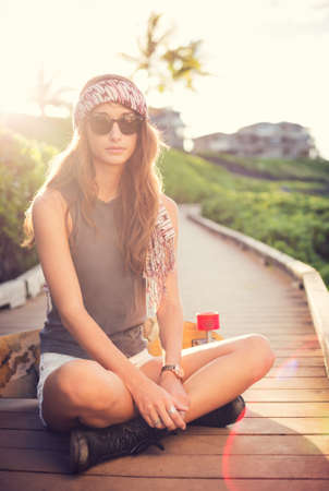 Fashion lifestyle, Beautiful young woman with skateboard, backlit at sunsetの写真素材