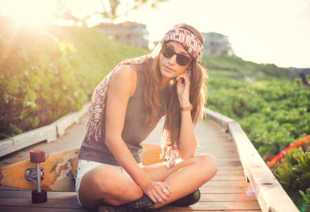 Fashion lifestyle, Beautiful young woman with skateboard, backlit at sunsetの写真素材