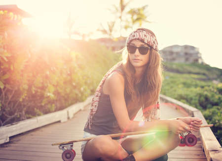 Fashion lifestyle, Beautiful young woman with skateboard, backlit at sunset