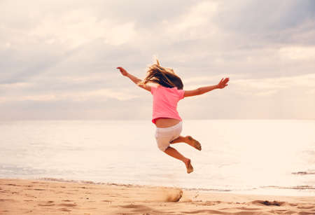 Happy Young Girl Jumping For Joy on the Beach at Sunset