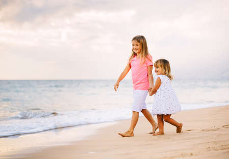 Adorable Young Sisters, Two Little Girls Walking together on the Beach at Sunet, Family Lifestyle.の写真素材