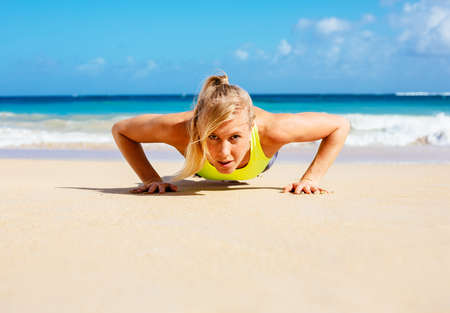Young attractive woman doing push ups outside. Fitness woman working out at the beach. Crossfit exercise. Fitness Concept.の写真素材