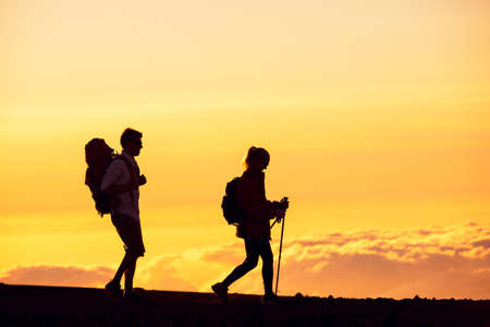 Silhouettes of two hikers with backpacks walking at sunset. Trekking and enjoying the sunset view from mountain top above the clouds.の写真素材