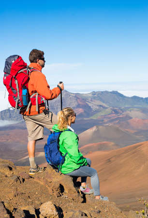 Two hikers relaxing enjoying the amazing view from the mountain top. Looking out over the volcano crater.の写真素材