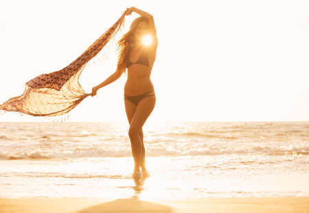 Free happy woman on beach at sunset. Beautiful relaxing walk on the beach. Fashion lifestyle, backlit, warm sunny colors.の写真素材