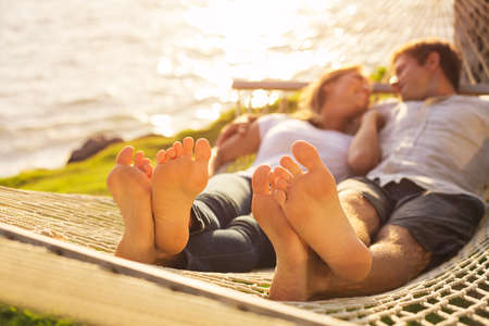 Romantic couple relaxing in tropical hammock at sunset, Shallow depth of field, focus on feet.の写真素材