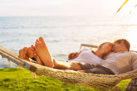 Romantic couple relaxing in tropical hammock at sunset, Shallow depth of field, focus on feet.の写真素材